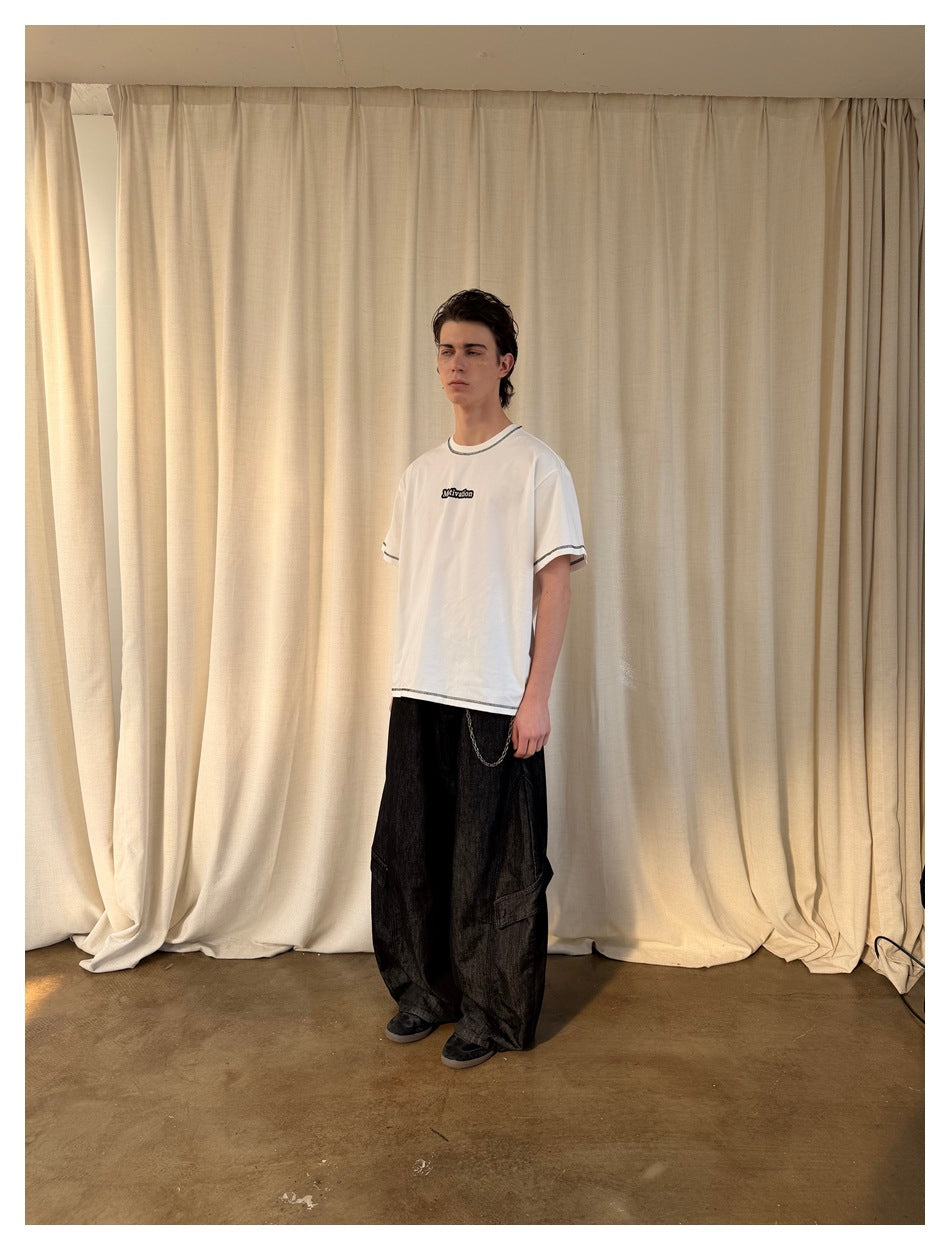 Model wearing the white t-shirt with dark contrast stitching and wide black cargo pants, side view