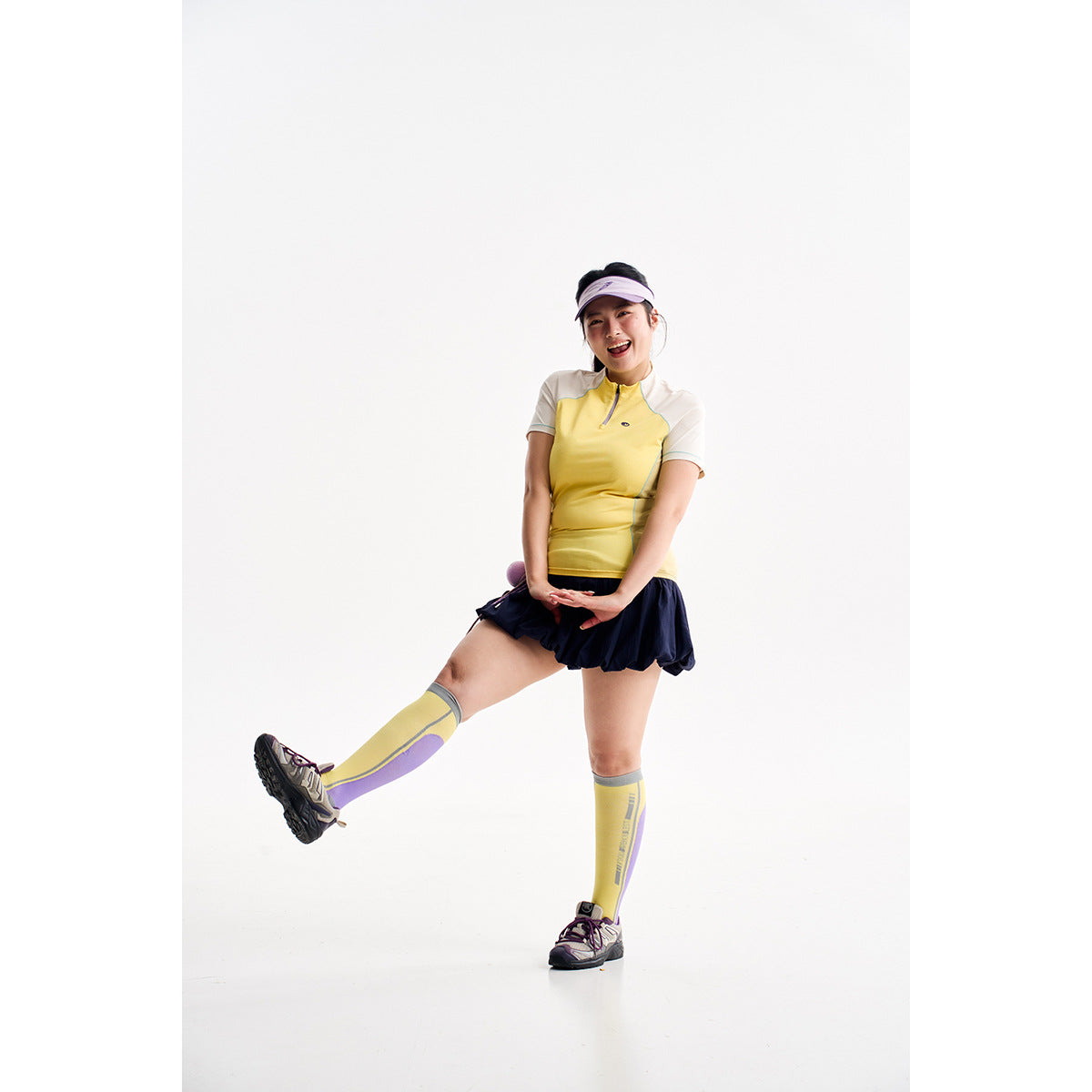 Model wearing a yellow and cream short-sleeve zip-neck top, navy skirt, and yellow knee-high socks.