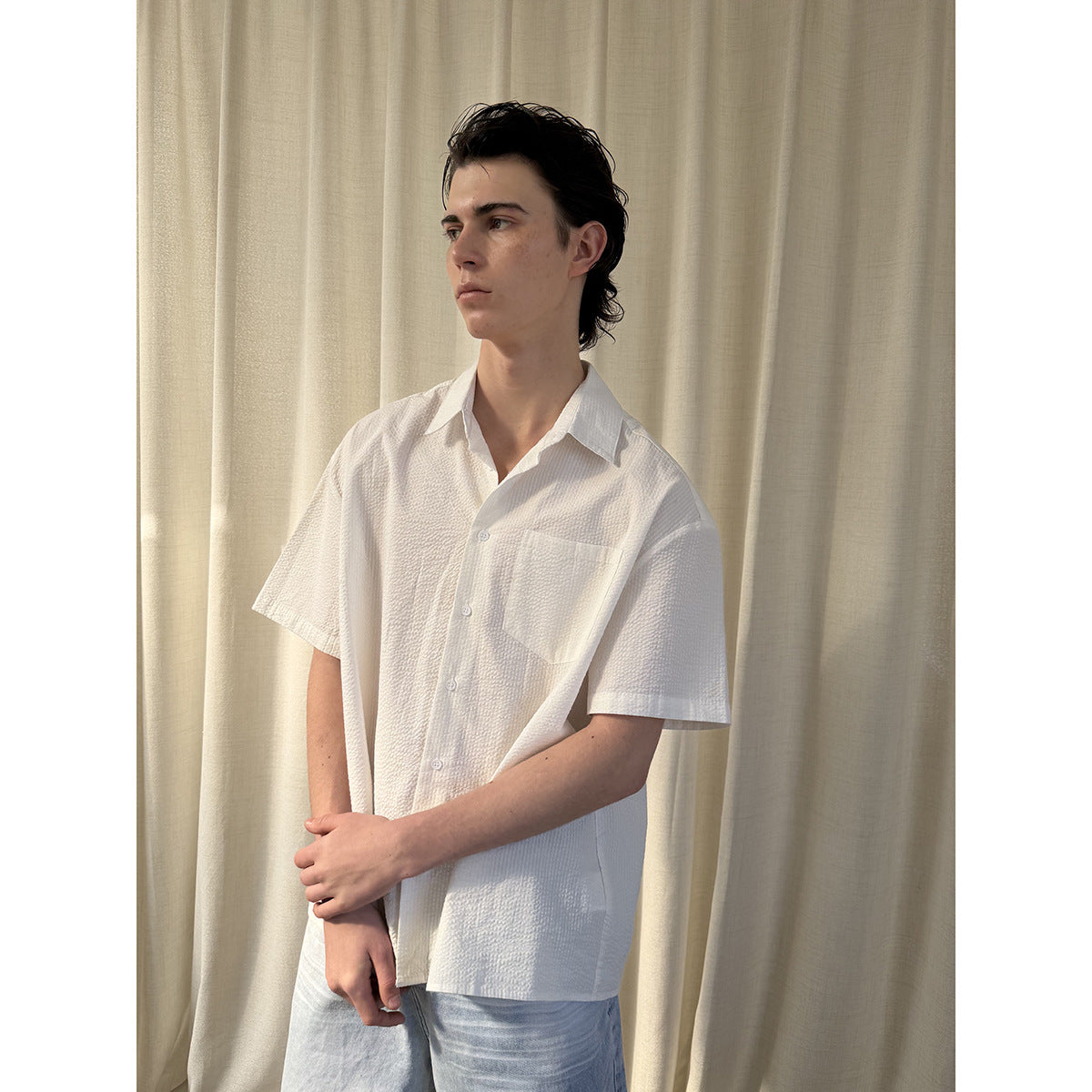 Model wearing a white short-sleeve button-up shirt with a collar and chest pocket, shown without a tie.