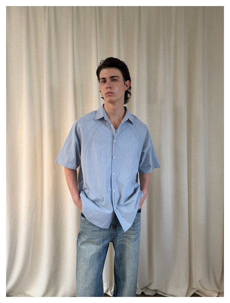 Front view of a person wearing a loose light blue striped short-sleeve shirt with contrast panels and jeans.