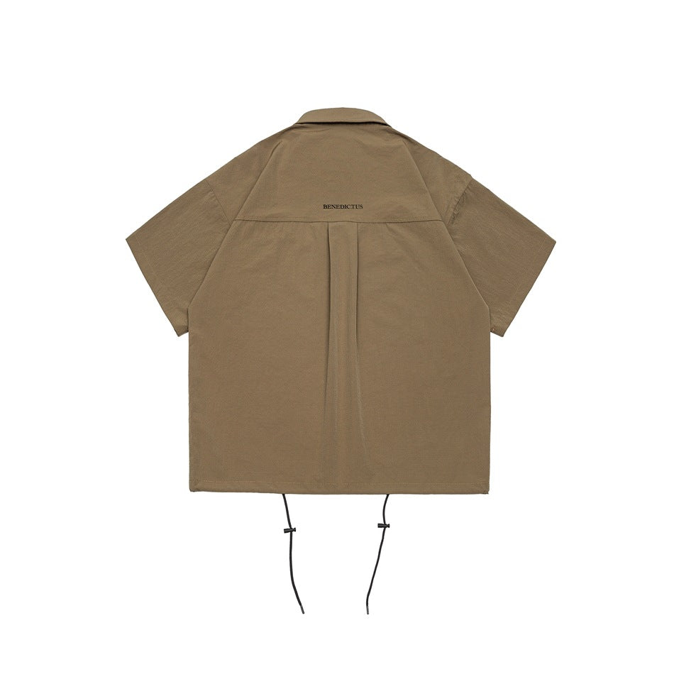Back view of a tan short-sleeve collared shirt with a center pleat and dangling hem cords.