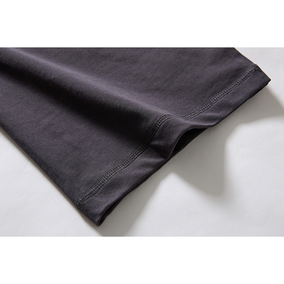 Close-up of a charcoal T-shirt sleeve edge with visible dark overlock stitching.