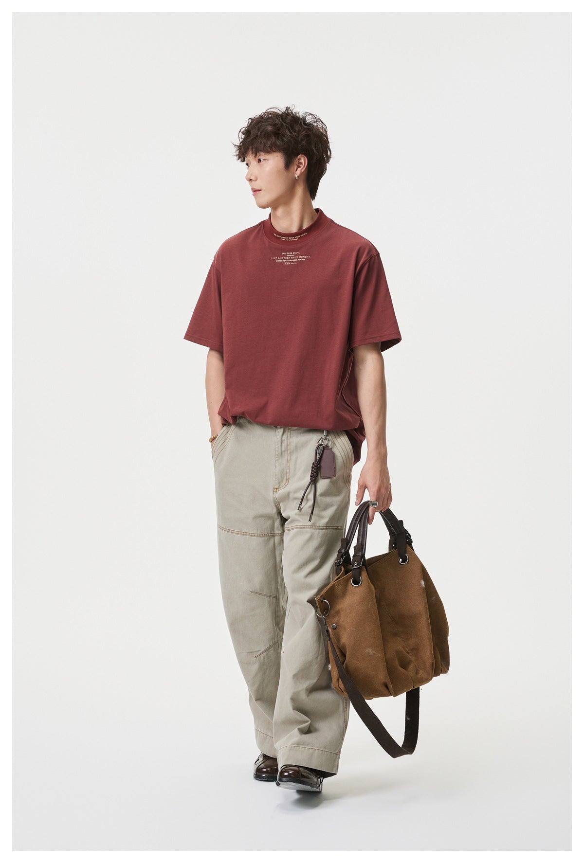 Model wearing a loose burgundy short-sleeve T-shirt with small white chest and collar text, paired with light trousers.
