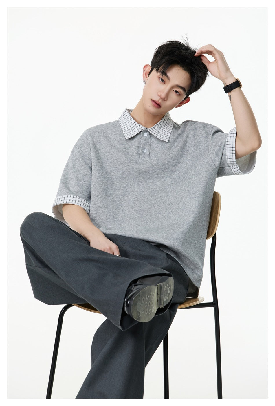 Model seated on a chair wearing a heather gray polo with plaid collar and cuffs, with gray wide-leg trousers