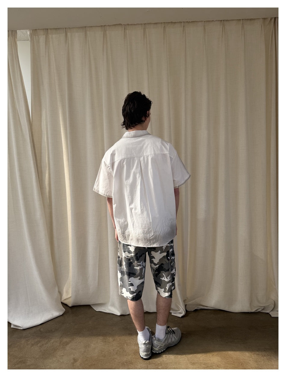 Model viewed from behind wearing a white short-sleeve button-up shirt.