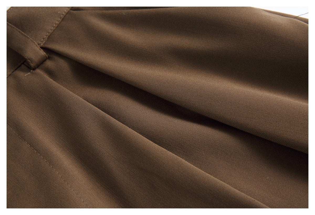 Close-up of brown trouser fabric showing a pleat and stitched seam.