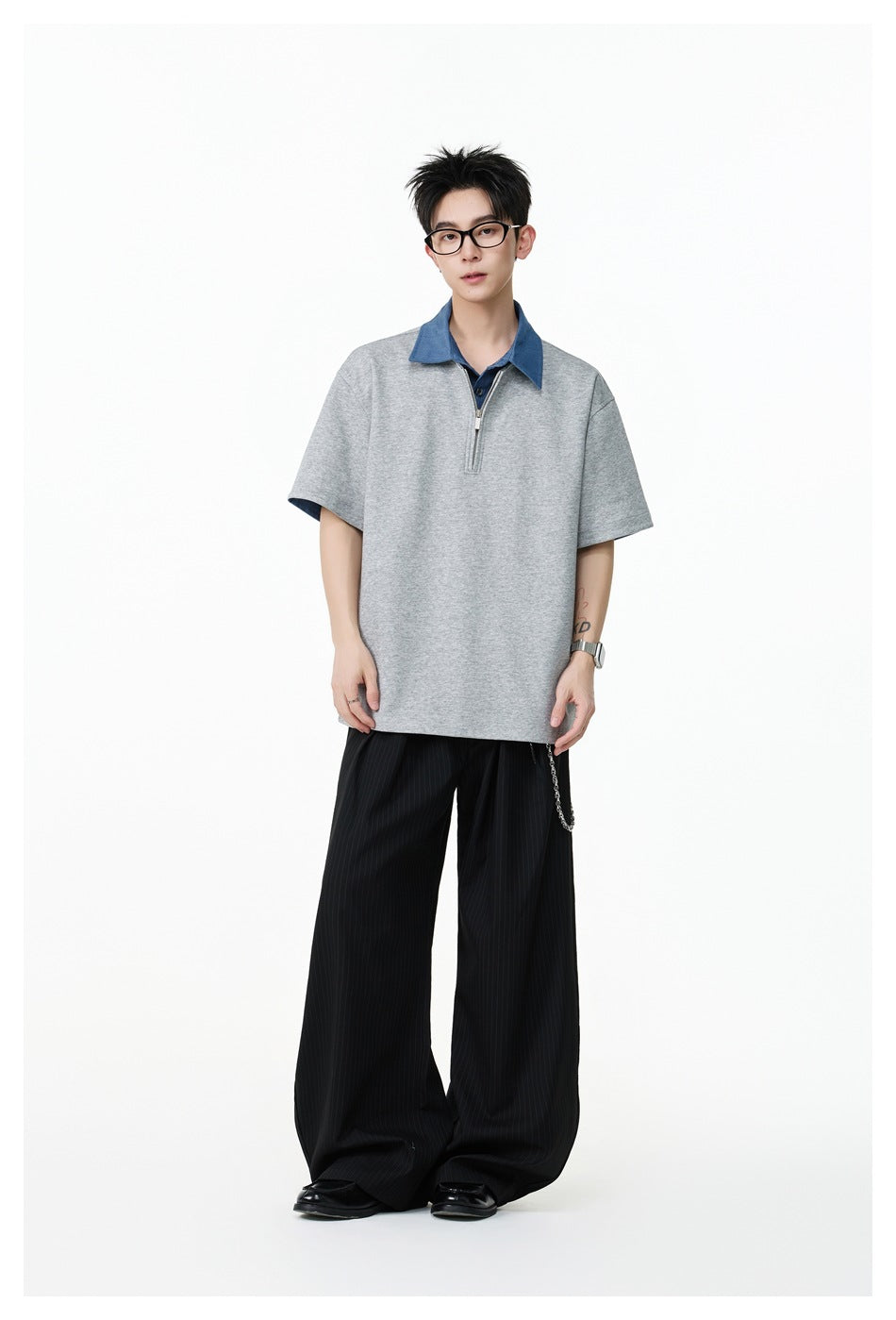 Model wearing an oversized gray short-sleeve top with a blue collar and quarter zip, paired with black wide-leg pinstripe