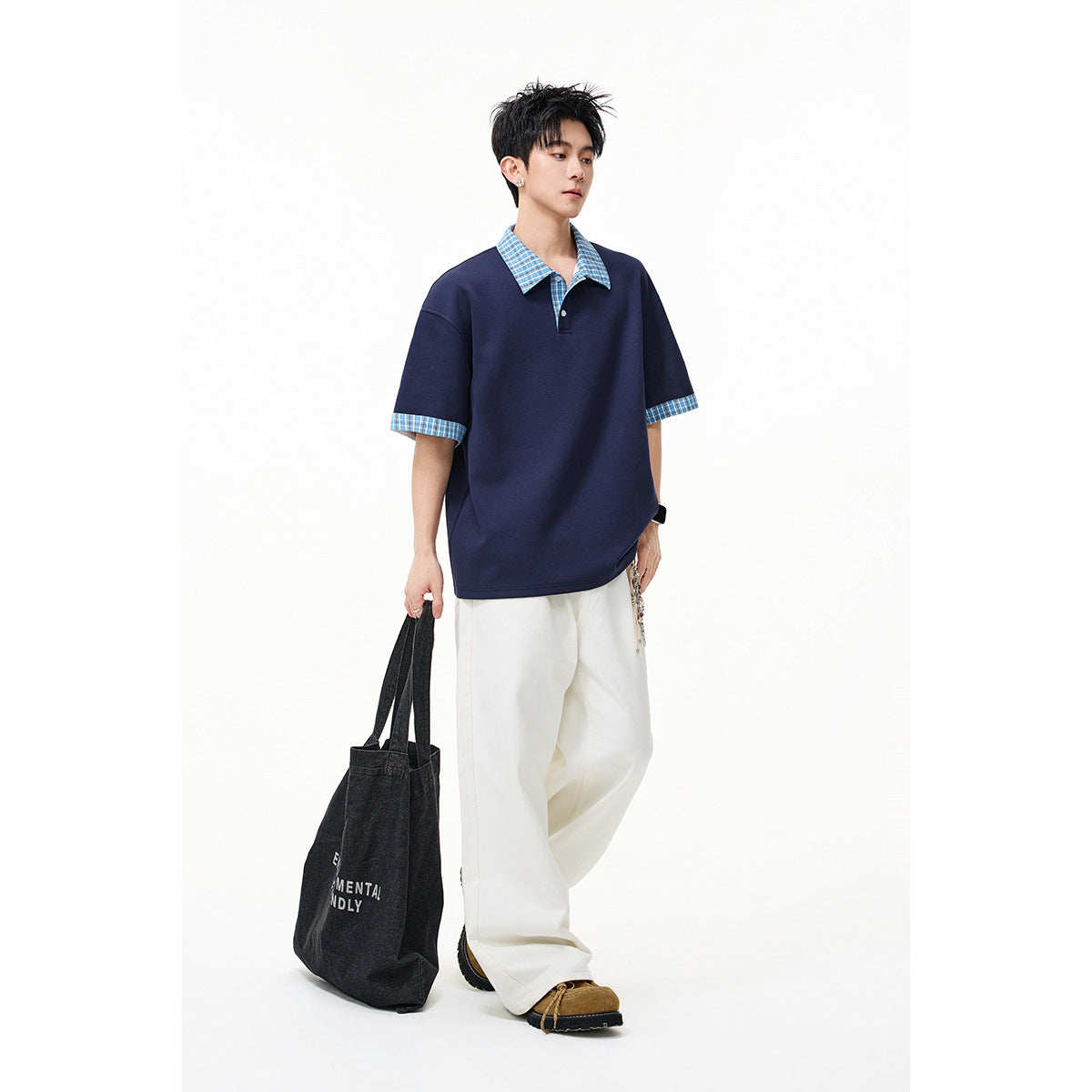 Model wearing a navy short-sleeve polo with blue checked collar and cuffs, styled with white trousers.