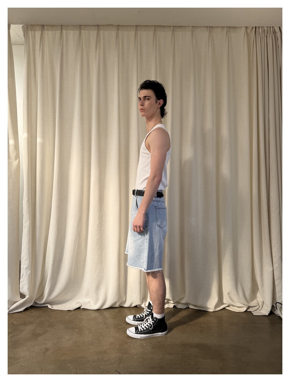 Side view of a model wearing a white tank top and light-wash frayed denim shorts.