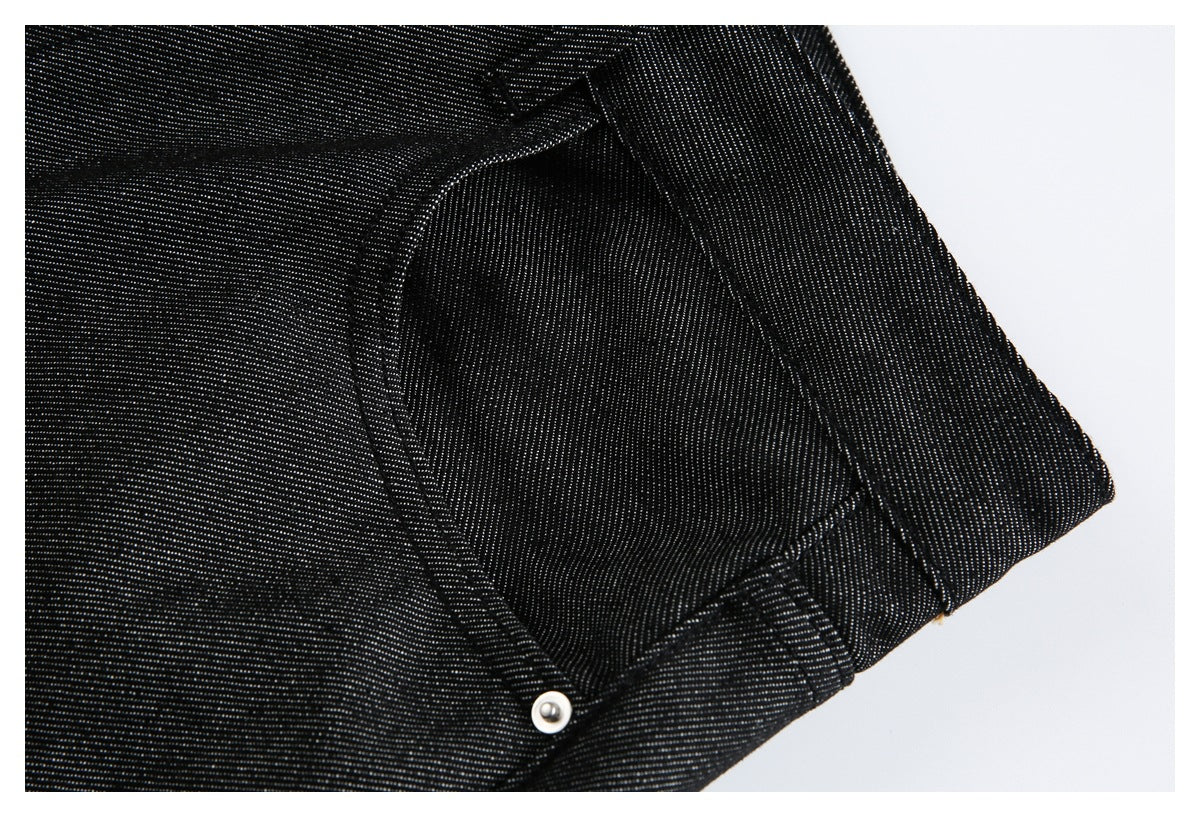 Close-up of black jeans with a curved pocket seam and small silver rivet.