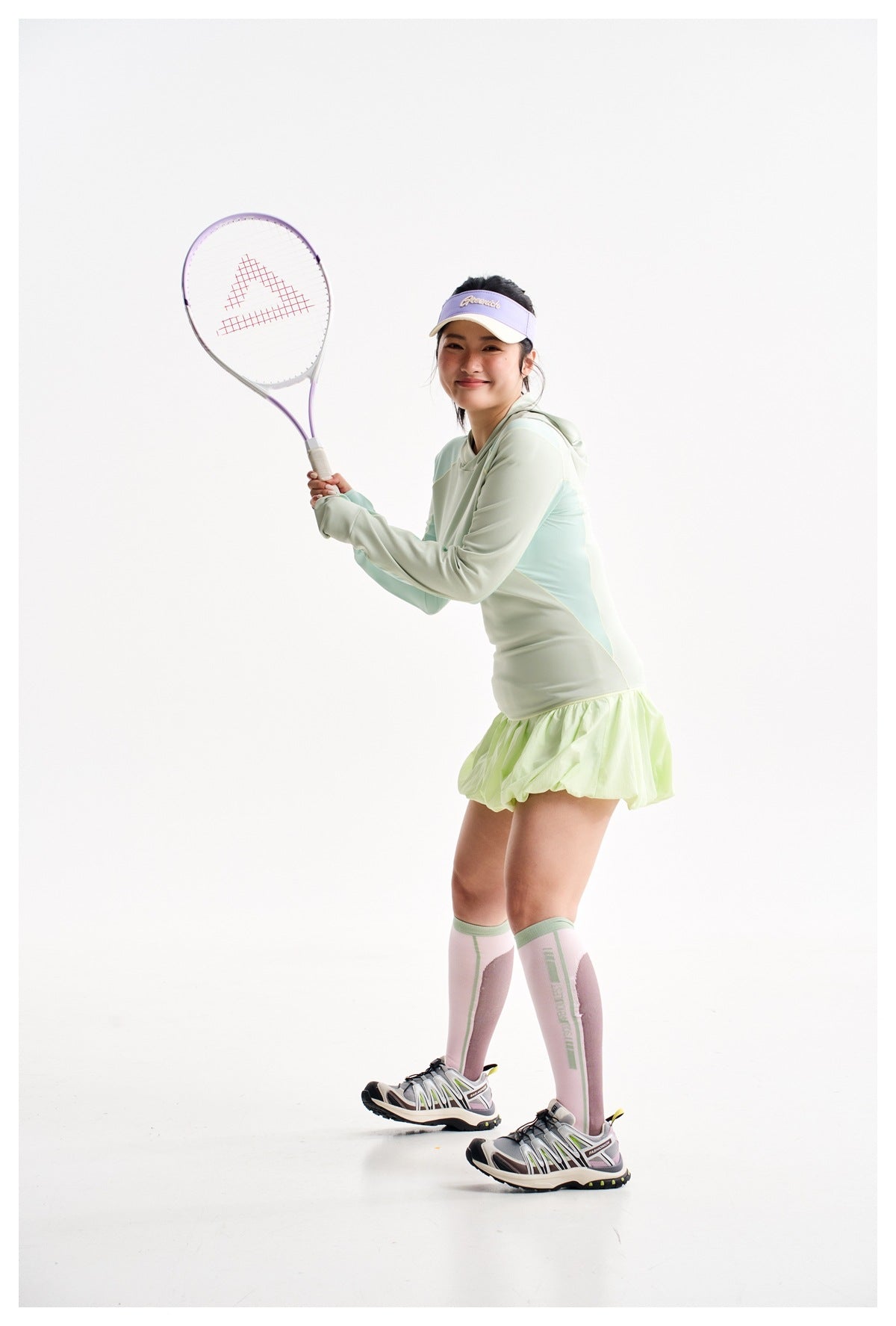 Model in a pale mint color-block hooded top and lime bubble-hem skirt, holding a tennis racket.