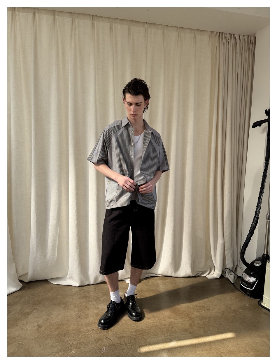 Model wearing a gray striped short-sleeve button-up shirt over a white tank, with black shorts.