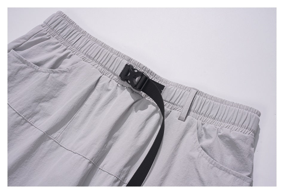 Close-up of light gray bottoms with an elastic waistband, black buckle strap, and curved pocket.