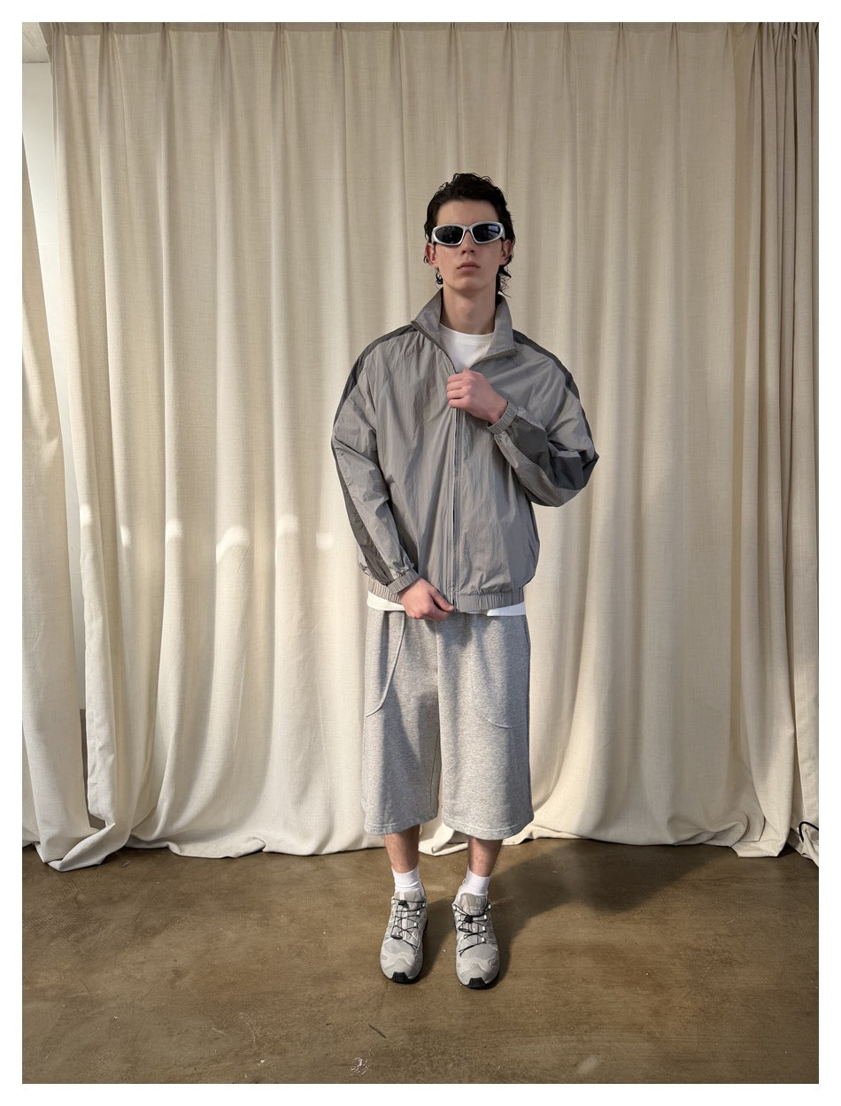 Full-length front view of a model wearing a light gray zip jacket with dark sleeve panels.