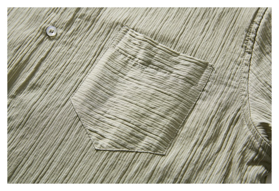 Close-up of a muted olive-gray shirt with a button and angular chest pocket in narrow textured stripes.