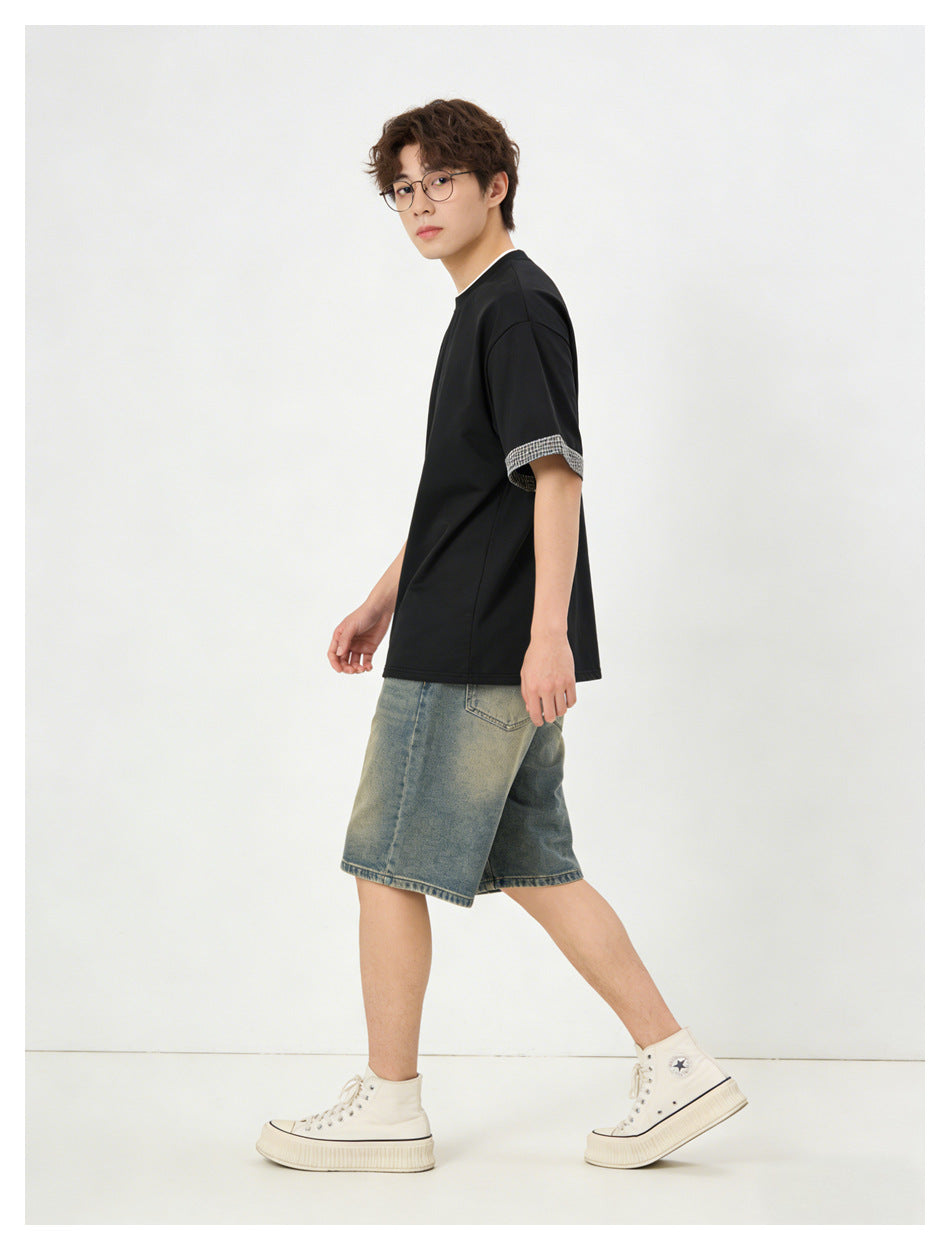Side view of a model wearing a black T-shirt with checked sleeve cuffs and blue denim shorts.