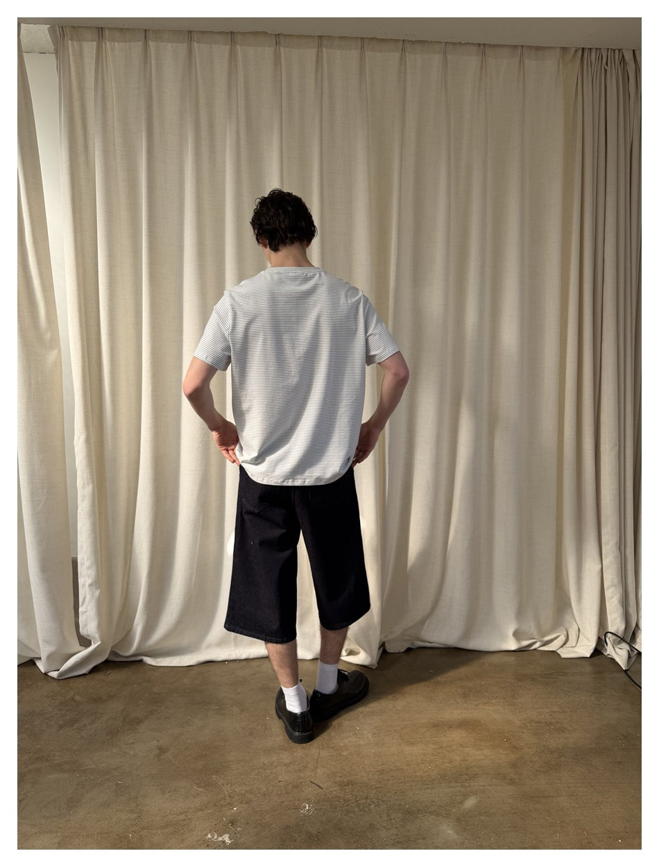 Rear view of a model wearing a white T-shirt with fine gray stripes and black knee-length shorts.