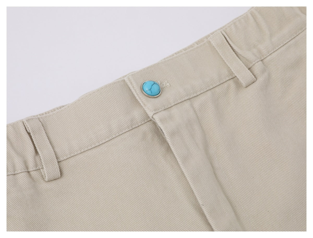 Close-up of beige trouser waistband with belt loops and a turquoise button.
