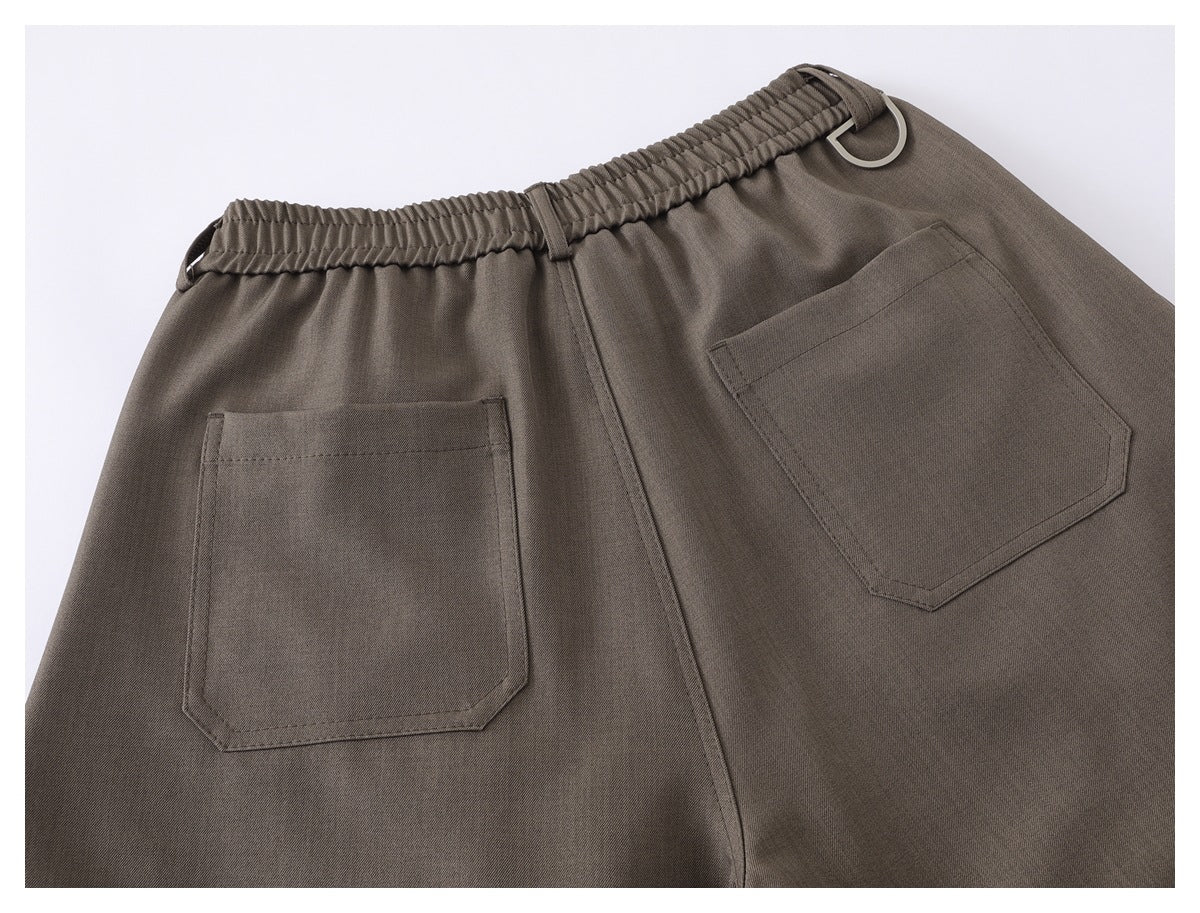 Back view of taupe trousers with a gathered elastic waistband, metal belt rings, and two patch pockets.