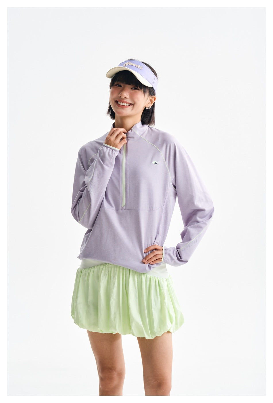 Model posing in a lilac quarter-zip top, pale mint bubble skirt and lavender visor.