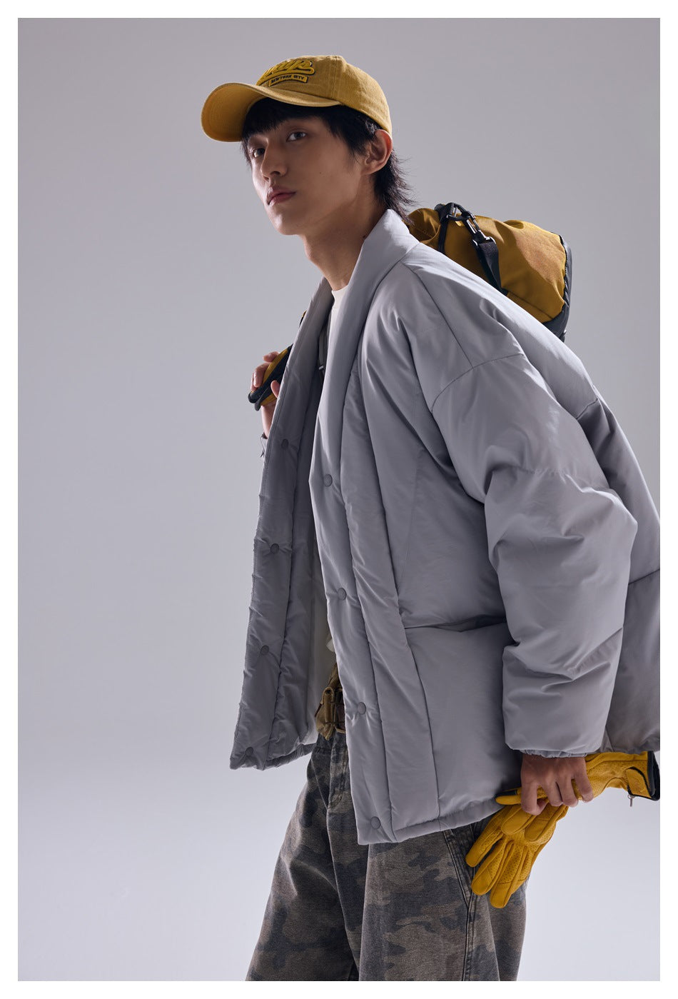 Side view of a model wearing a light gray oversized quilted jacket with snap buttons and large pockets.