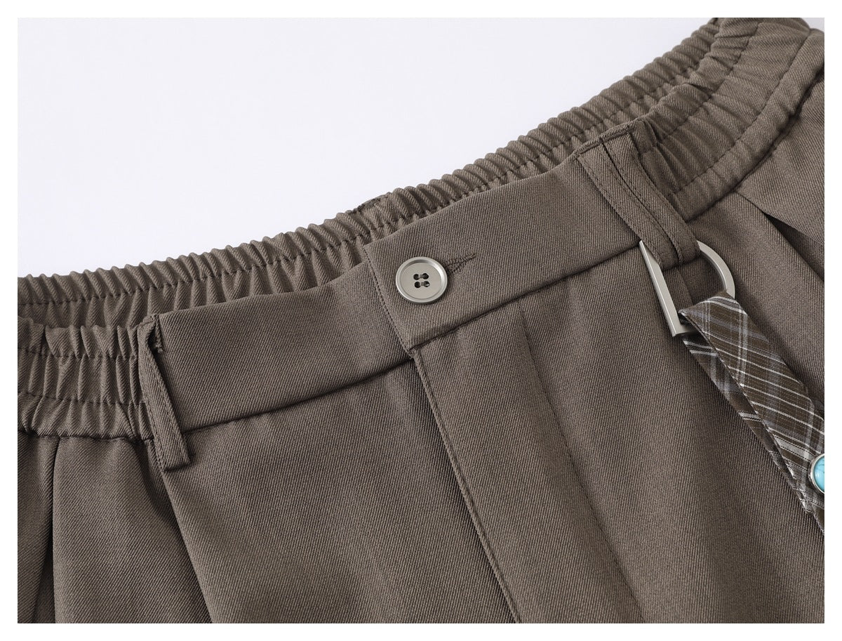 Close-up of taupe shorts showing the elastic waistband, button closure, belt loops, and plaid hanging strap.