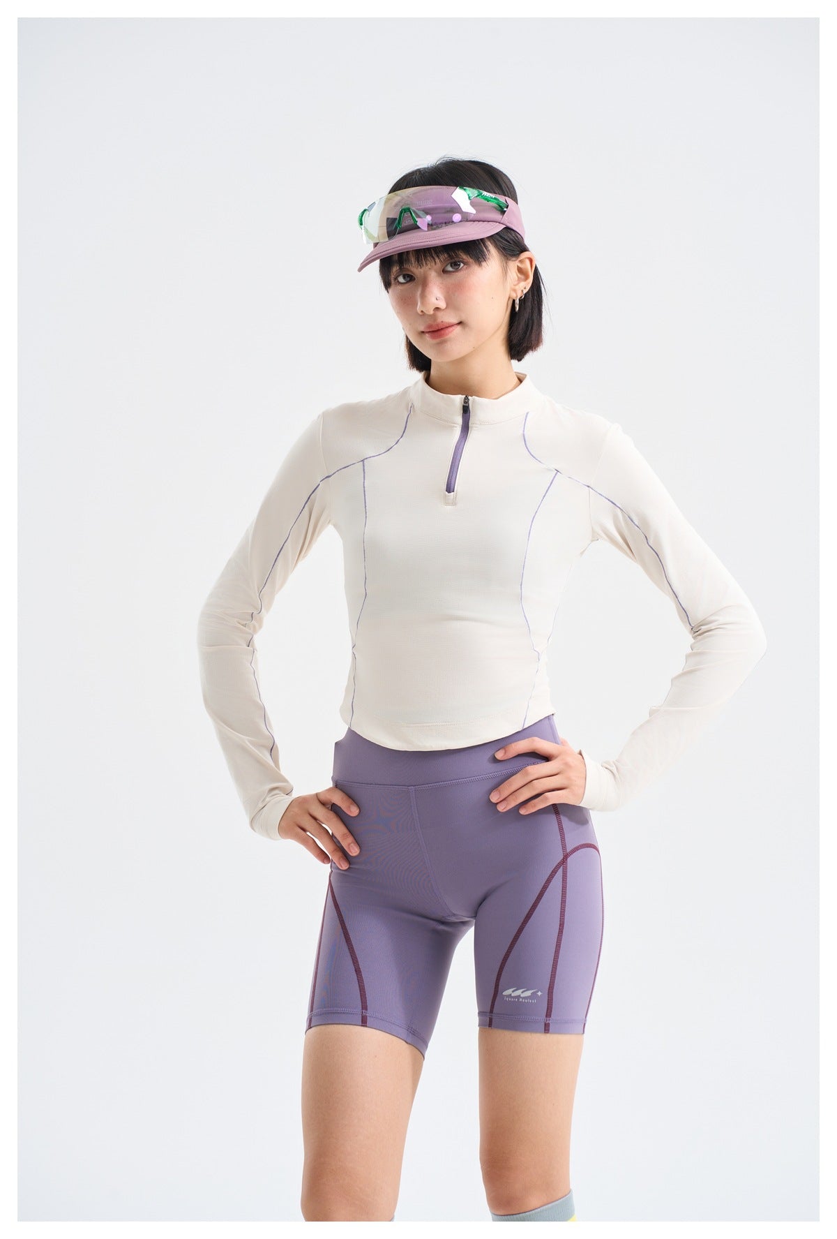 Close view of a model wearing an ivory quarter-zip top with lavender seam detailing and lavender cycling shorts.