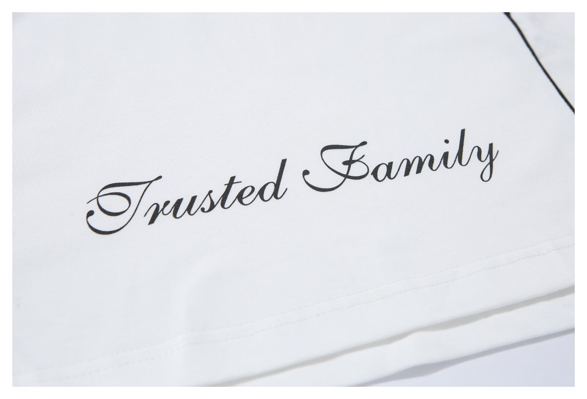 Close-up of the words “Trusted Family” printed in black script on the white T-shirt.