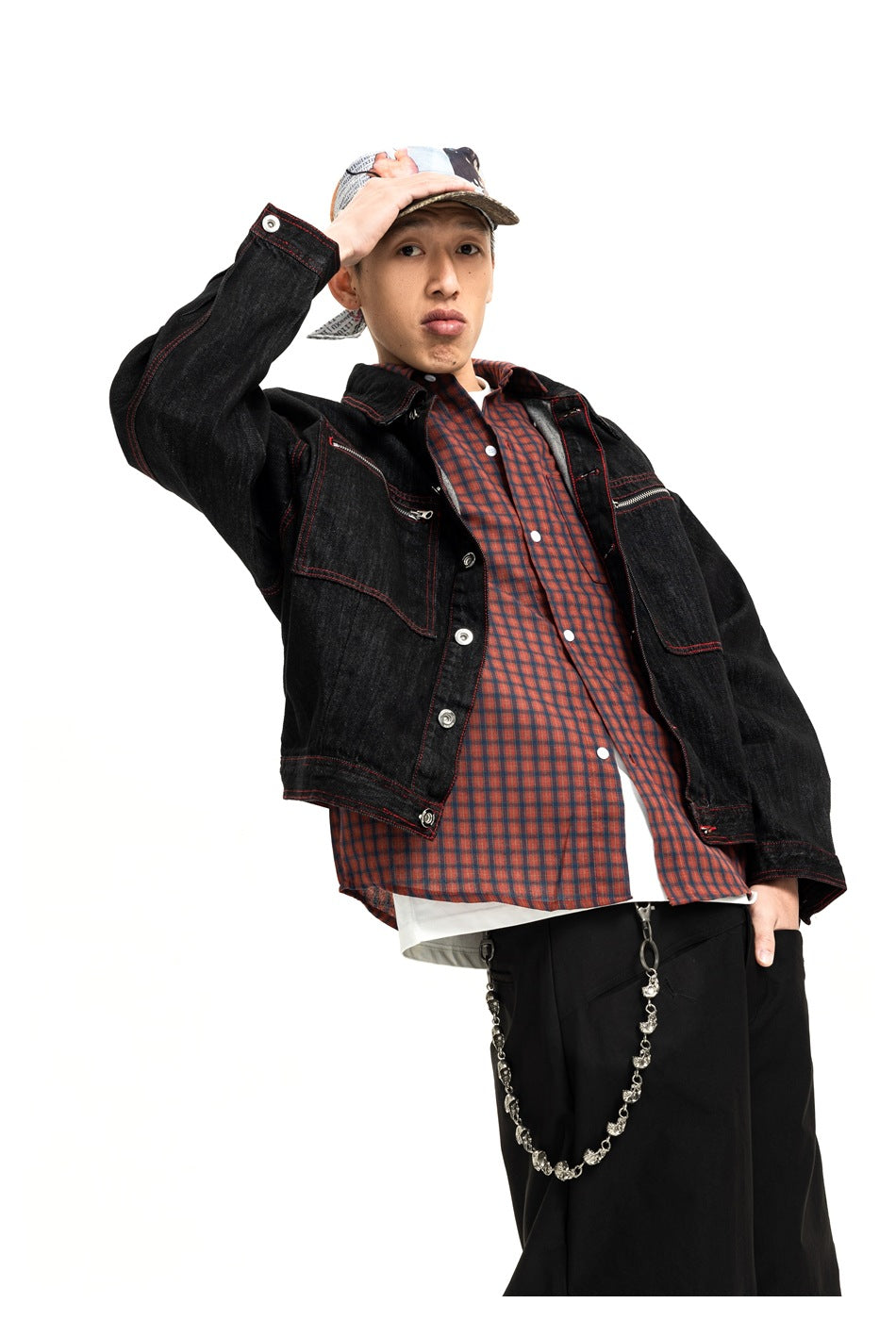 Model wearing an open black jacket with red stitching over a red plaid shirt and white undershirt.