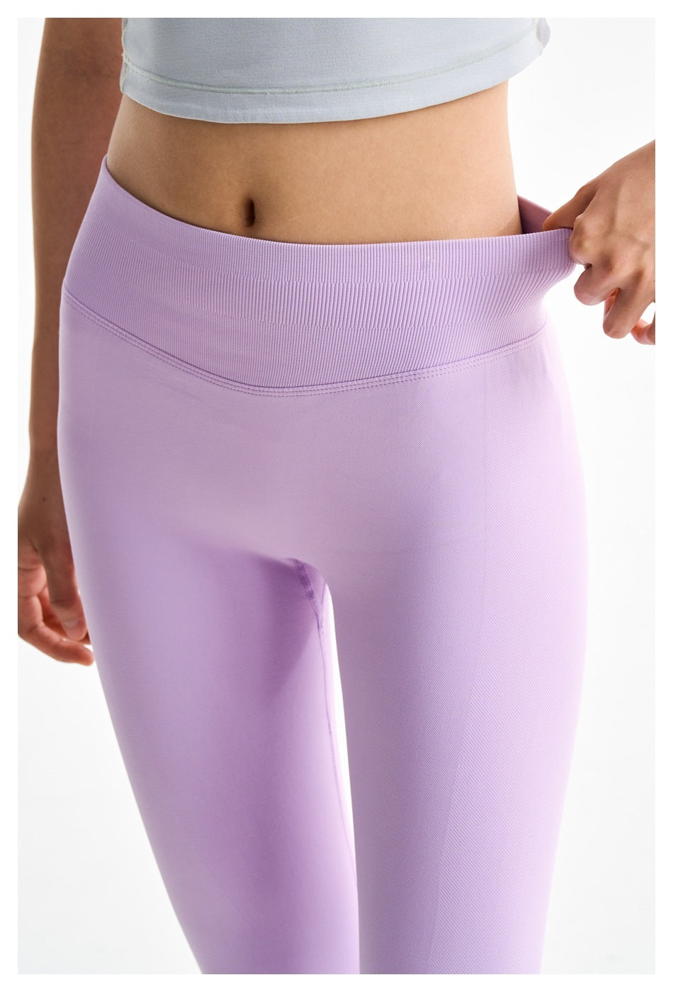 Close-up of lilac leggings with a wide ribbed waistband being stretched outward by hand.