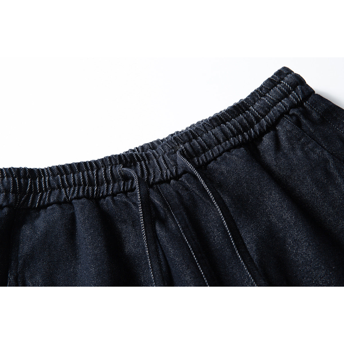Close-up of dark indigo pants showing a gathered elastic waistband and front stitching.