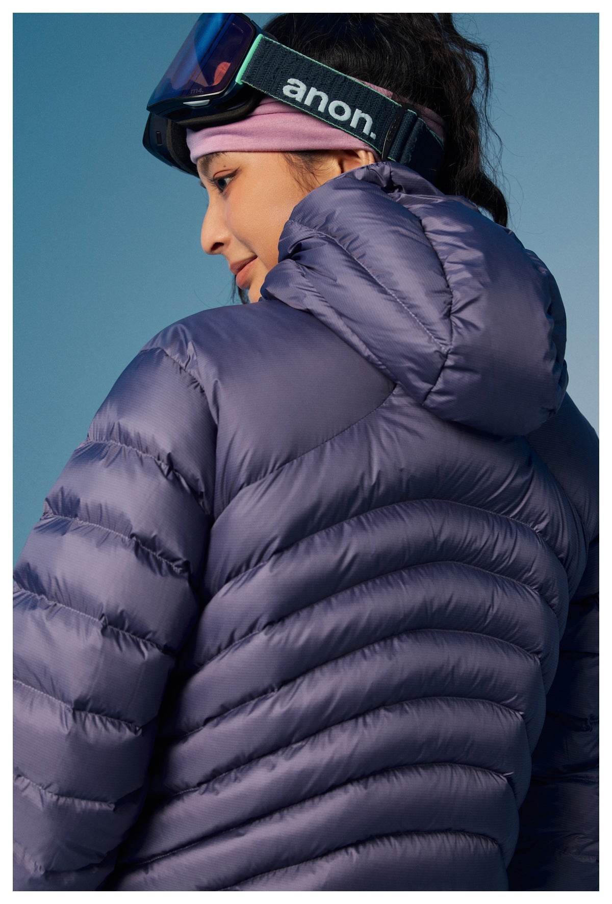 Close-up of a woman wearing a lavender puffer jacket with a high padded collar and hood.