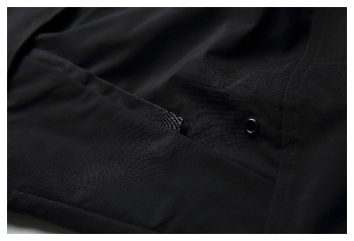 Close-up of black fabric showing a folded flap, stitched seam, and a black eyelet.