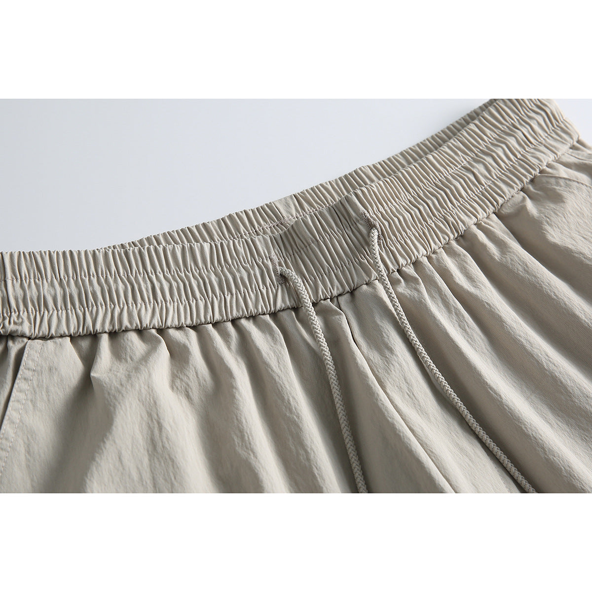 Close-up of light beige shorts showing a wide gathered elastic waistband and braided drawstrings.