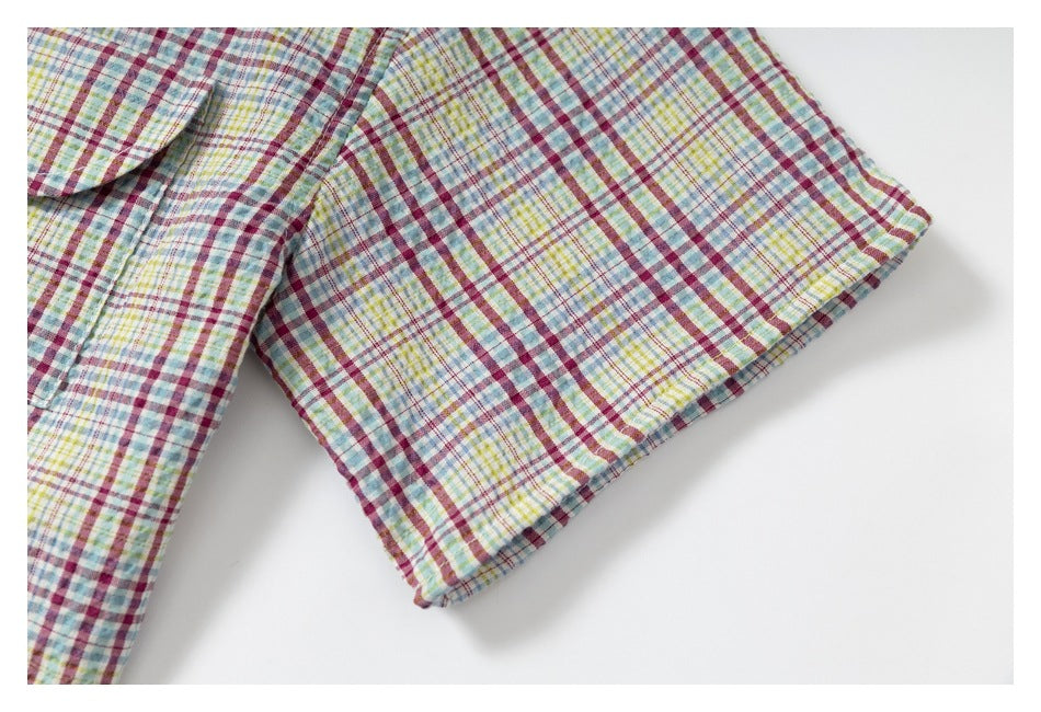 Close-up of a short sleeve and hem on a multicolor plaid shirt laid flat.
