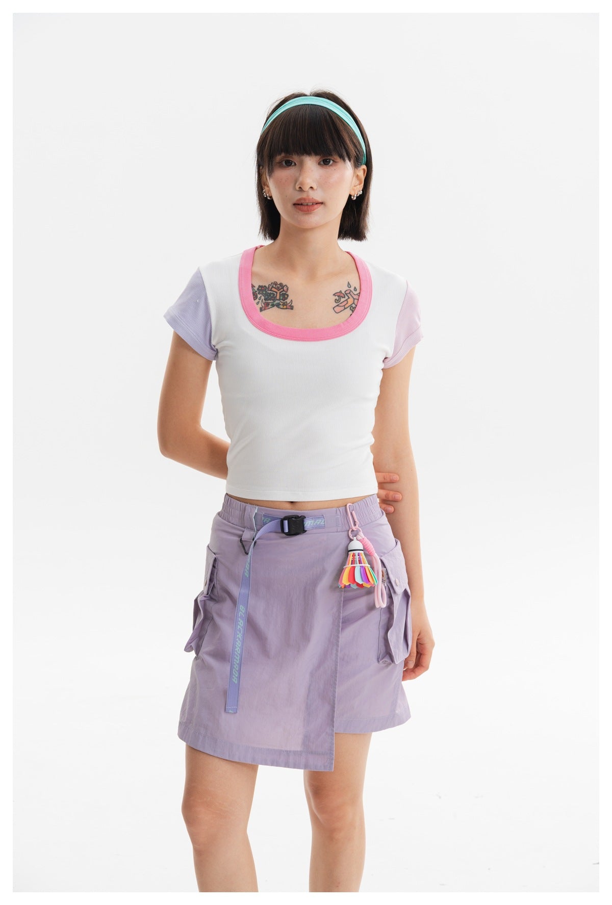 Model wearing a white crop top with pink neckline and lilac sleeves, paired with a lavender cargo skirt.