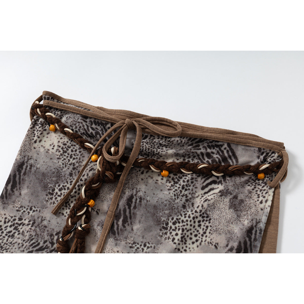 Close view of the gray animal-print skirt's brown tie waist, braided trim, and small orange beads.