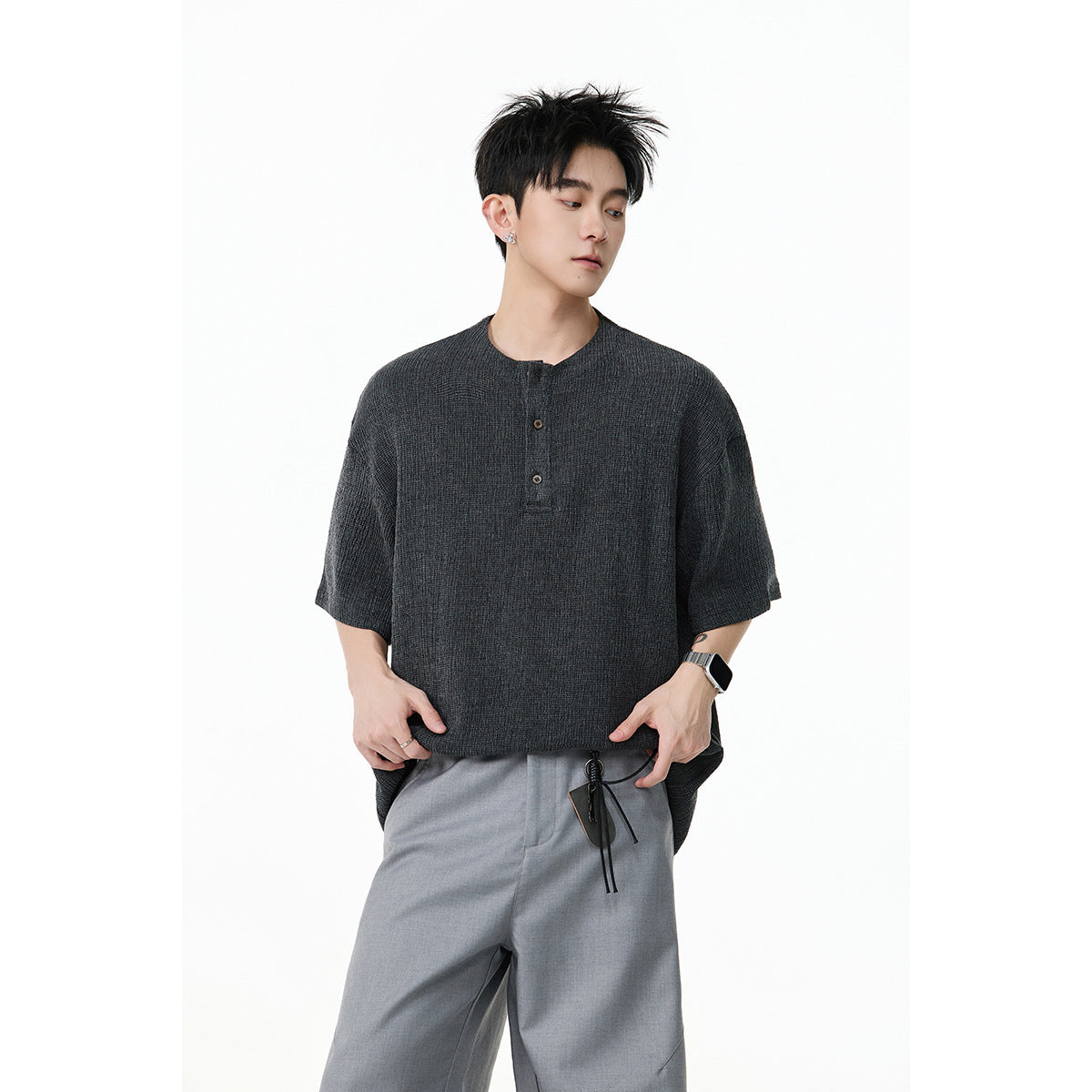 Model wearing a charcoal short-sleeve henley shirt with a three-button placket and loose gray trousers.