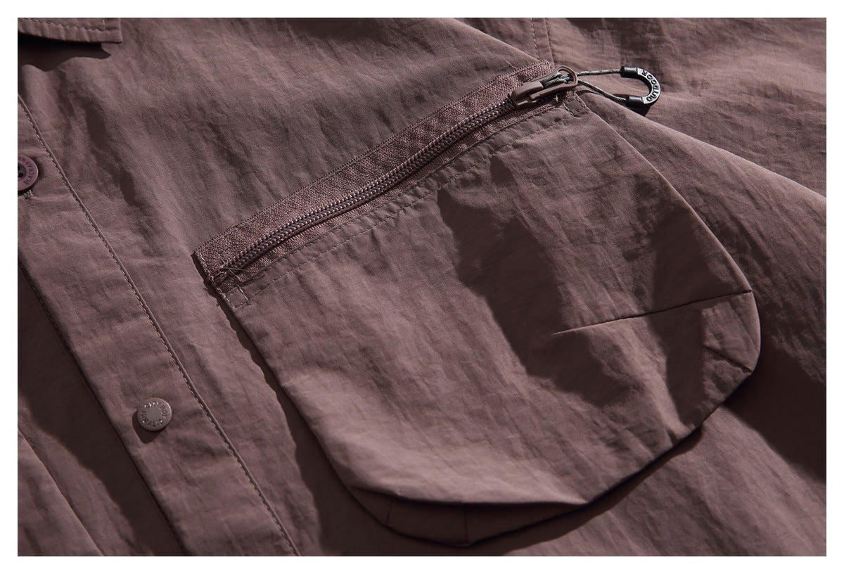 Close-up of a brown jacket's large zip pocket, with a dark zipper pull and snap-button placket.
