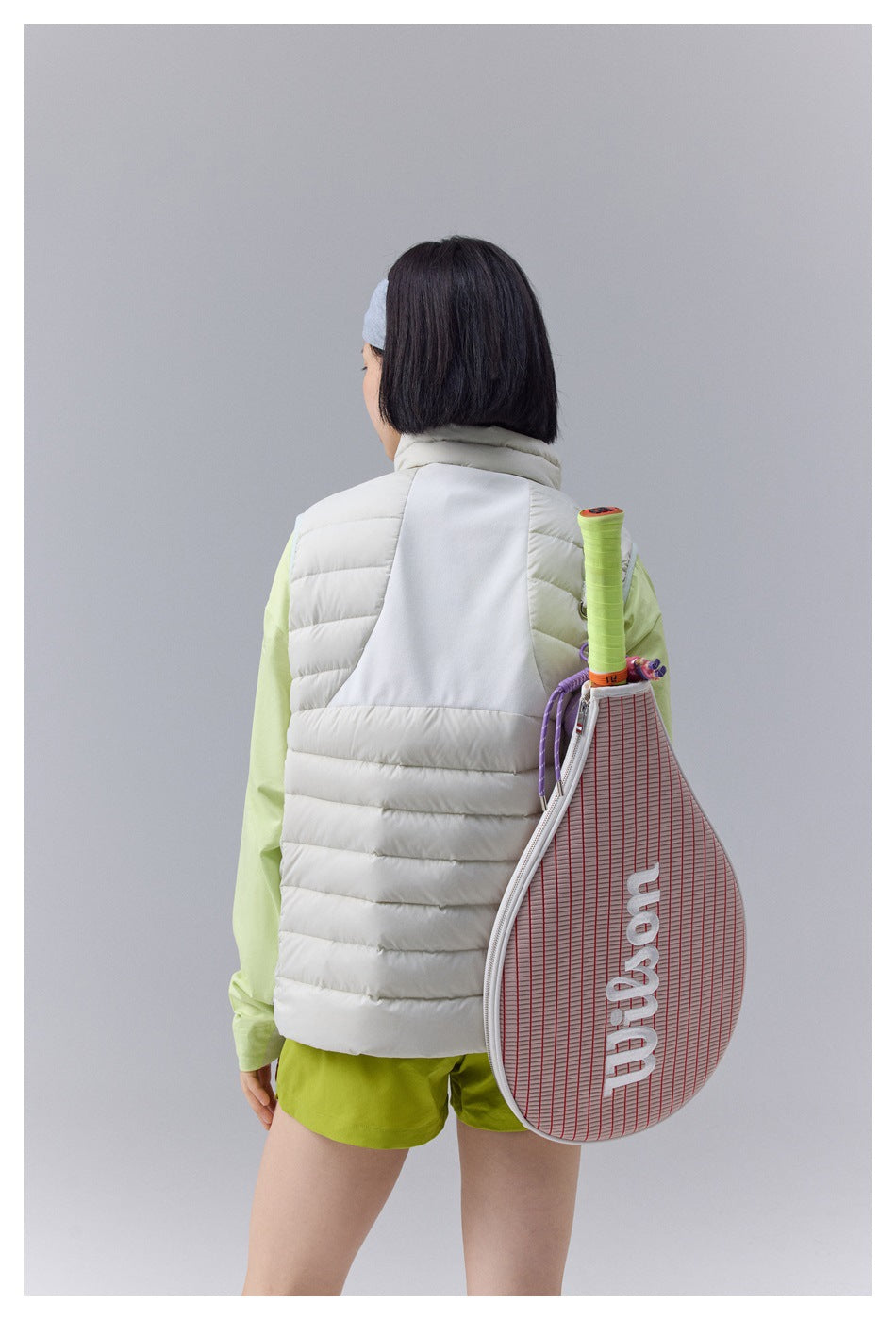 Rear view of a woman wearing a white quilted vest with a contrasting white upper-back panel.