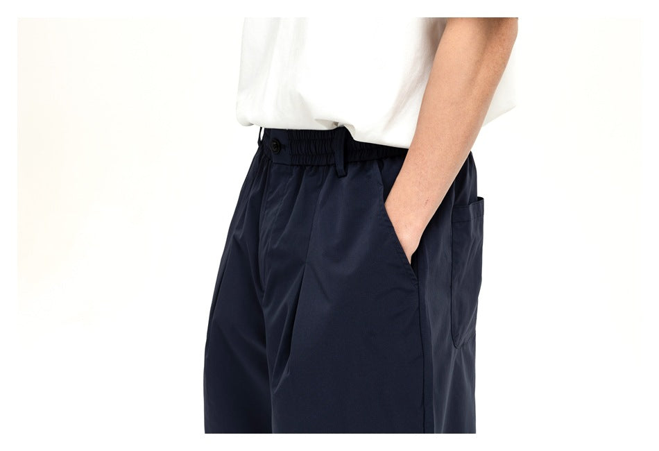 Close view of a model wearing dark navy shorts, showing the elastic waistband, button, side pocket, and rear pocket.