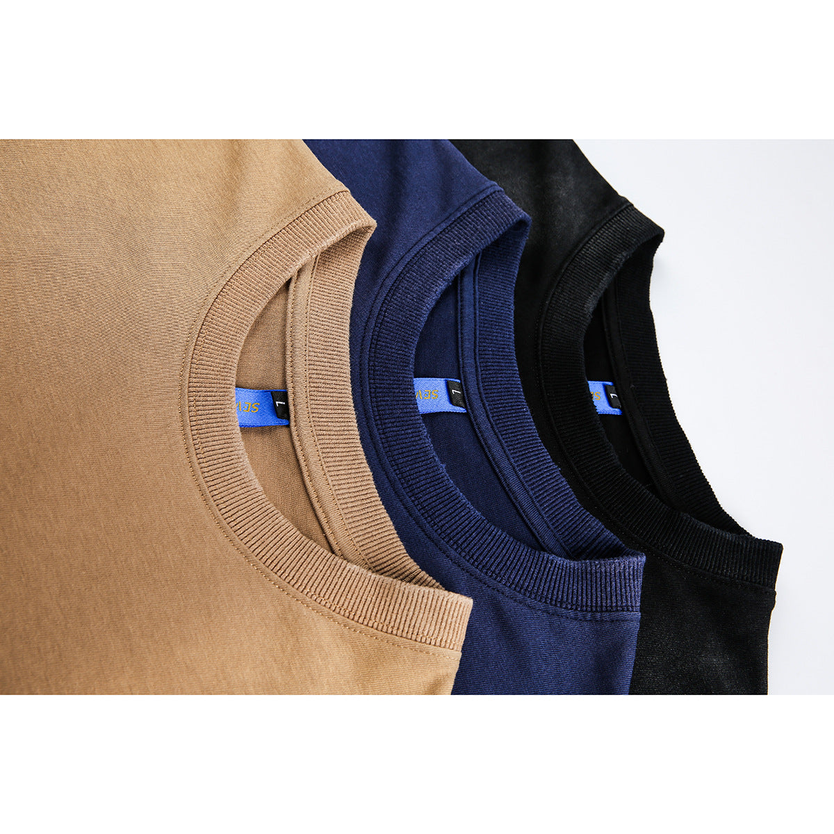 Close-up of ribbed crew necklines and inner labels on tan, navy, and black T-shirts.