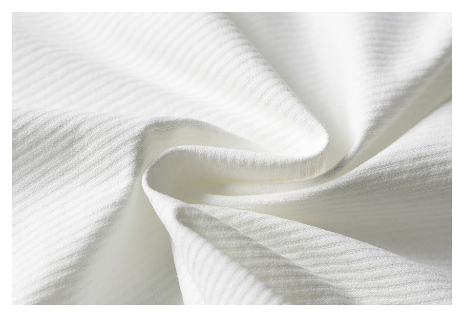White ribbed knit fabric draped into soft folds, showing its texture.