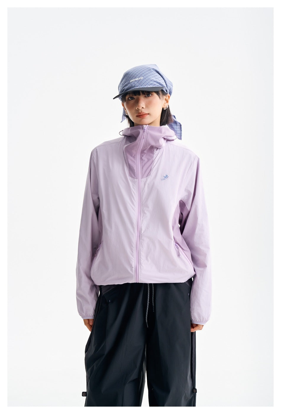 Front view of a model in a lilac hooded zip jacket with black pants and a blue plaid cap.
