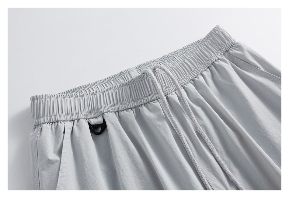 Close-up of light gray shorts showing a gathered elastic waistband, drawstring, and small black loop.