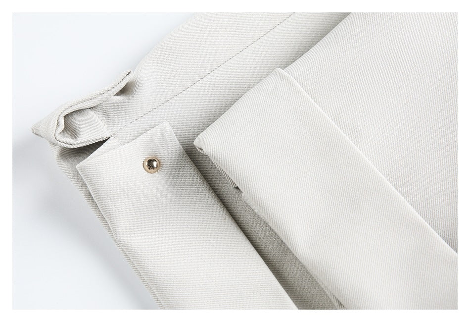 Close-up of a light ivory garment tab with a metal snap beside folded fabric panels.