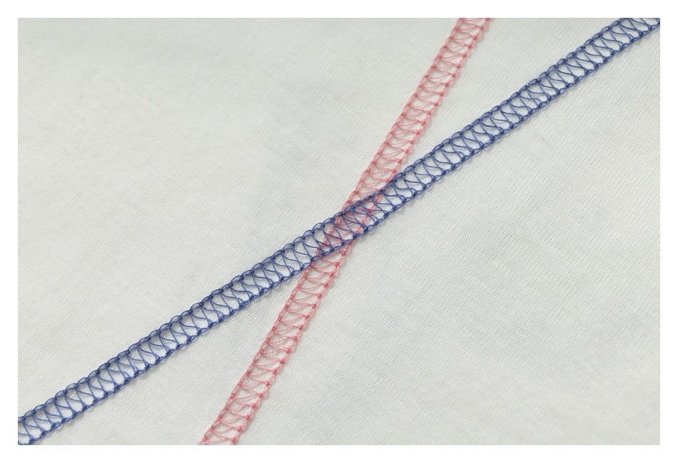 Close-up of pink and blue overlock stitching crossing on pale fabric.