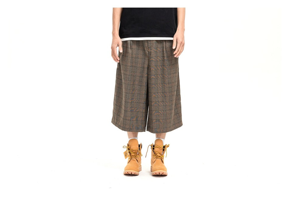 Front view of brown-gray plaid wide-leg shorts on a model, paired with a black shirt and tan boots.
