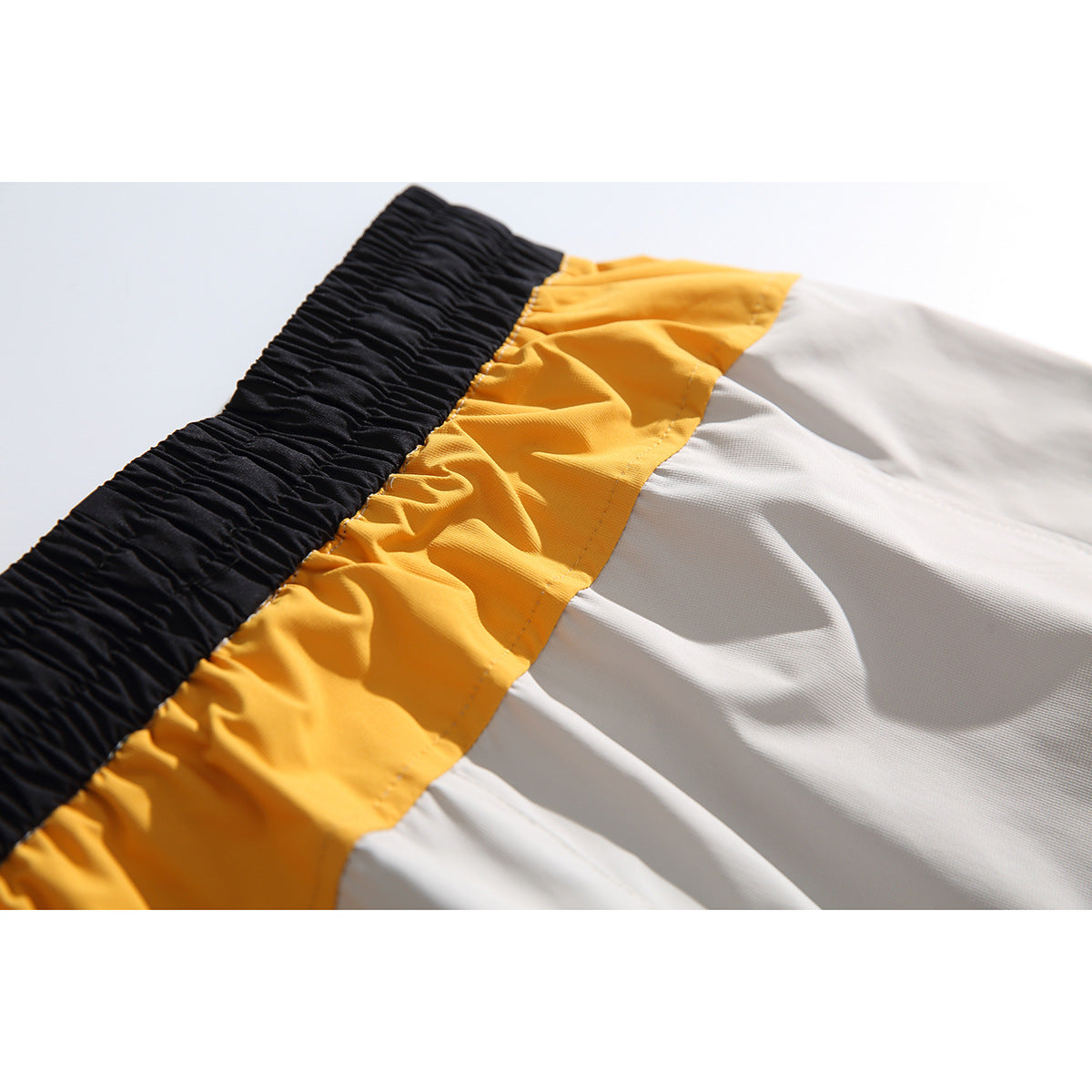 Close-up showing the black elastic waistband, mustard-yellow panel, and light gray fabric of the shorts.