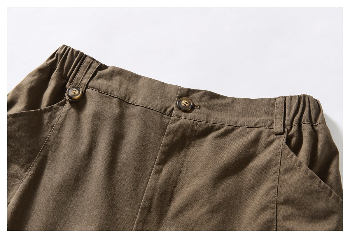 Close-up of brown shorts showing the buttoned waistband, side elastic, belt loops, and angled front pocket.
